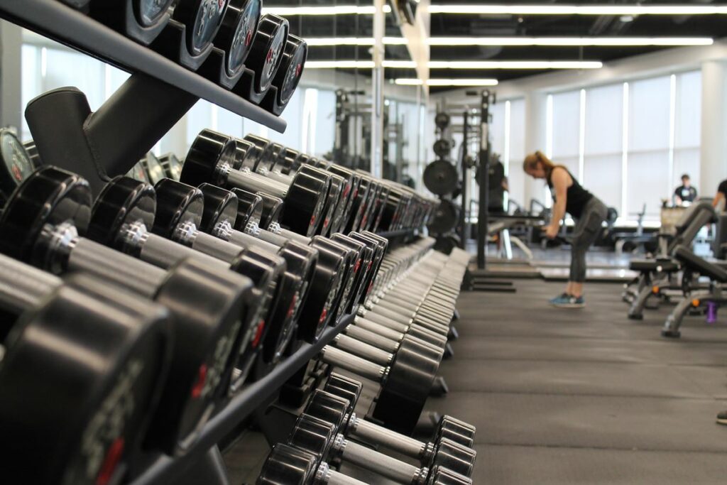 Halteres de academia e no fundo mulher fazendo exercícios 