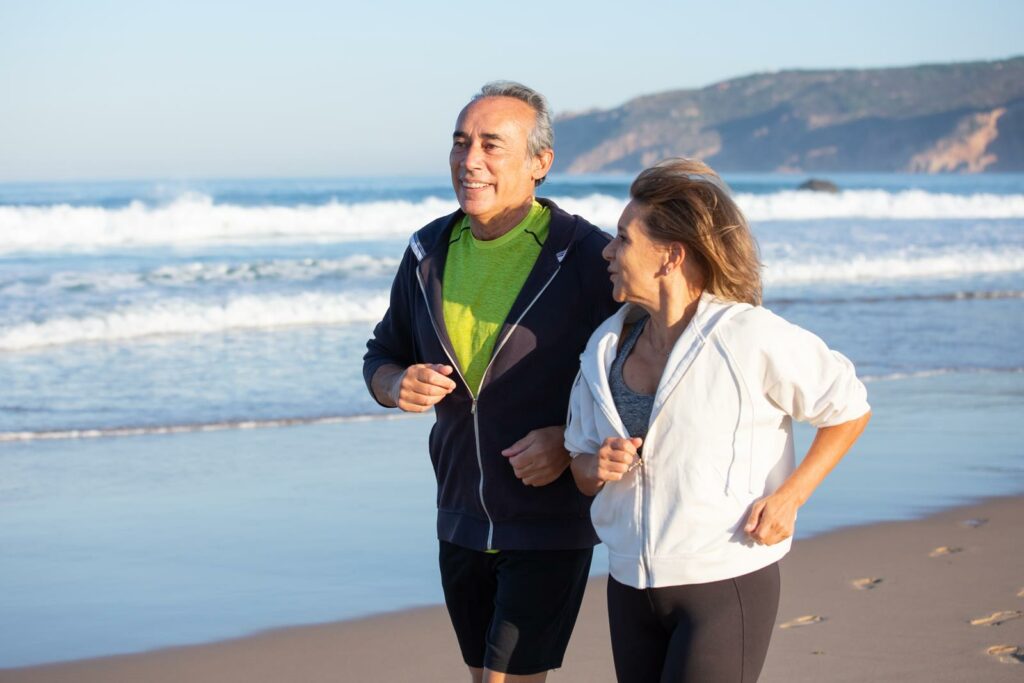 A foto mostra um casal idoso caminhando na praia