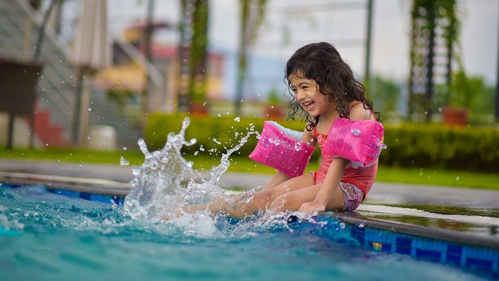 Criança sentada na beira de piscina e batendo os pés na água