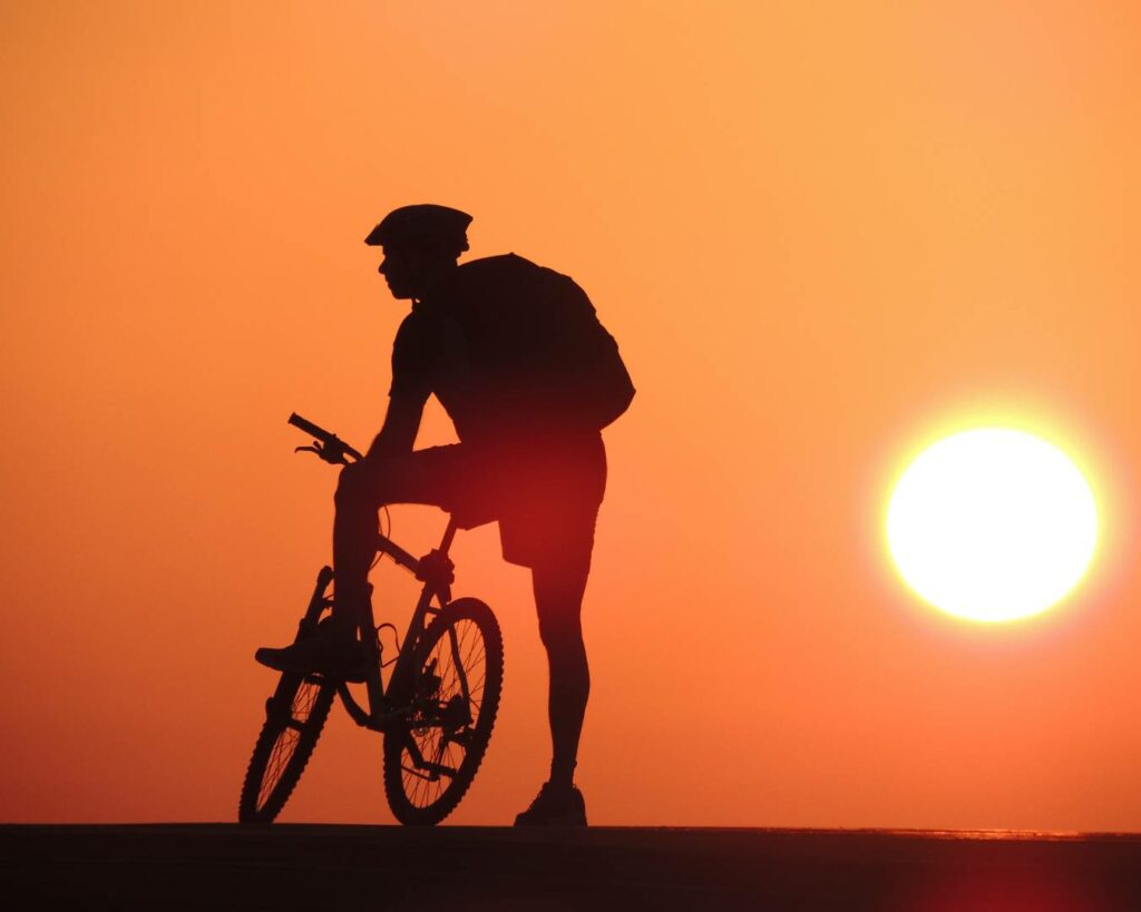 Sombra de homem com bicicleta e sol ao fundo
