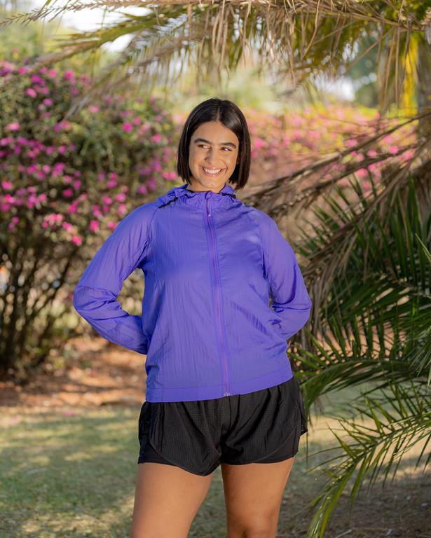 Mulher com jaqueta de corrida roxa e shorts pretos num parque